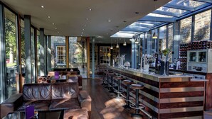 A modern bar area with a wooden bar counter, multiple stools, and a seating area with a sofa and a coffee table. - Mosborough Hall Hotel, BW Signature Collection (Sheffield)