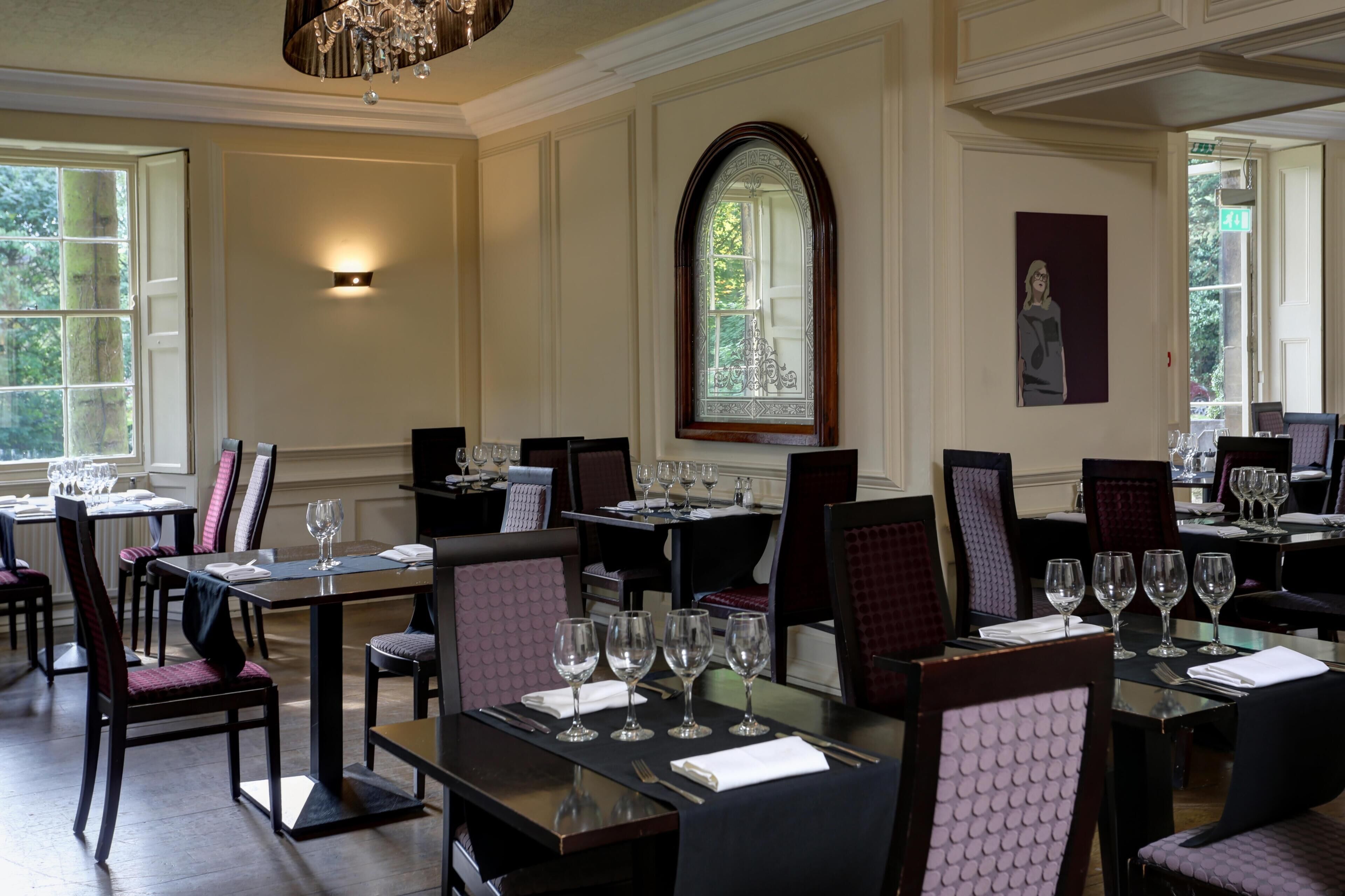 A restaurant with tables set for dining, a chandelier, and a large arched window.