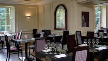A restaurant with tables set for dining, a chandelier, and a large arched window.