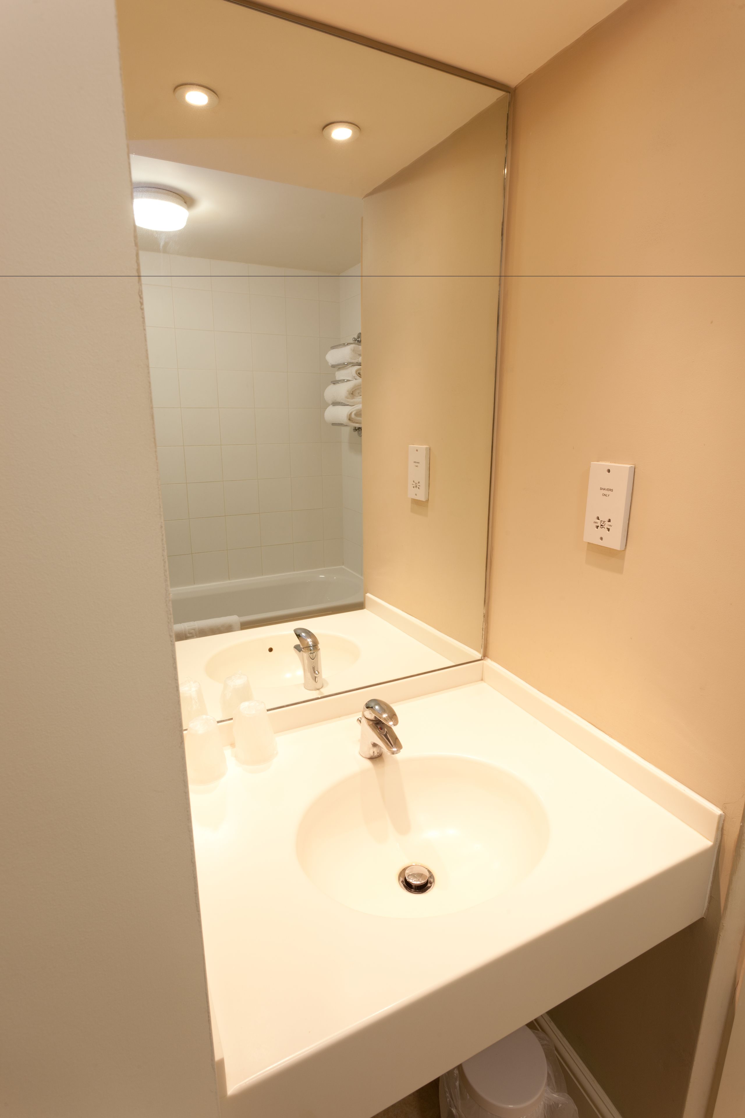Une salle de bain avec un lavabo blanc, un miroir et une douche visible au fond.