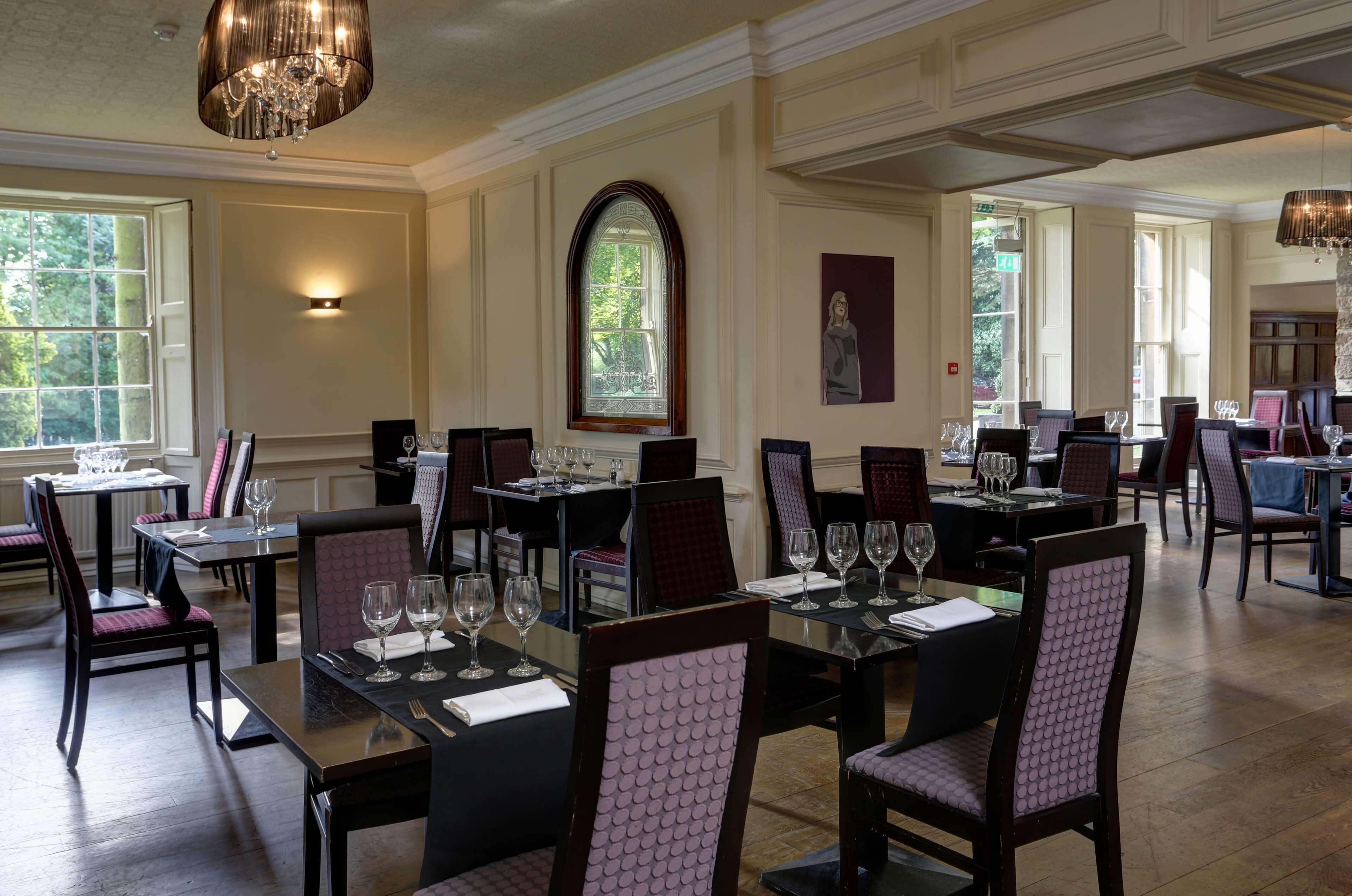 A dining area with tables set for service, large windows, and a chandelier.