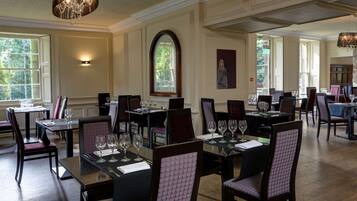 A dining area with tables set for service, large windows, and a chandelier.