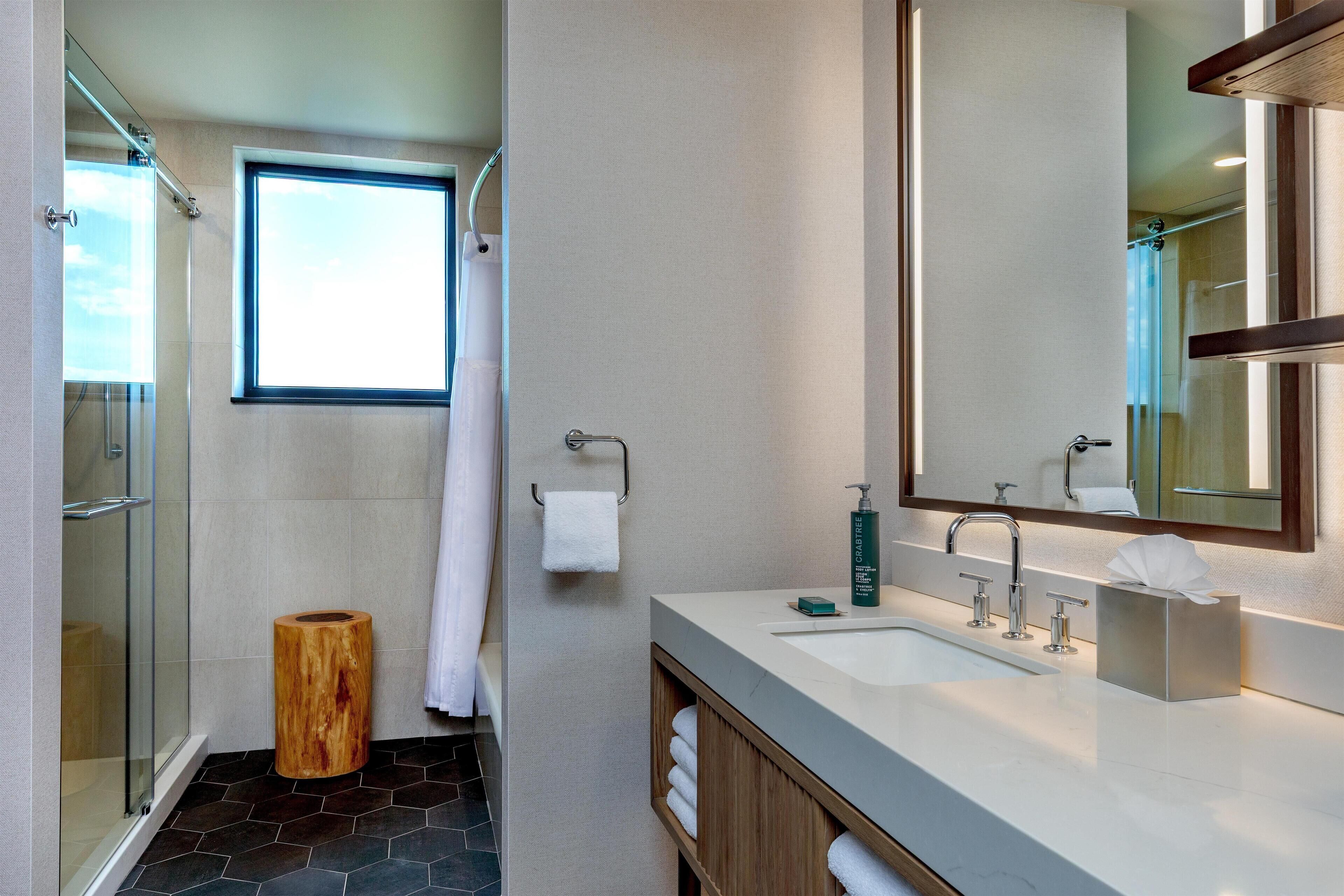A modern bathroom with a glass shower enclosure, a large mirror, and a white sink with a wooden vanity.