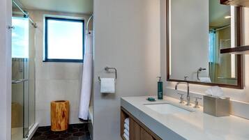 A modern bathroom with a glass shower enclosure, a large mirror, and a white sink with a wooden vanity.