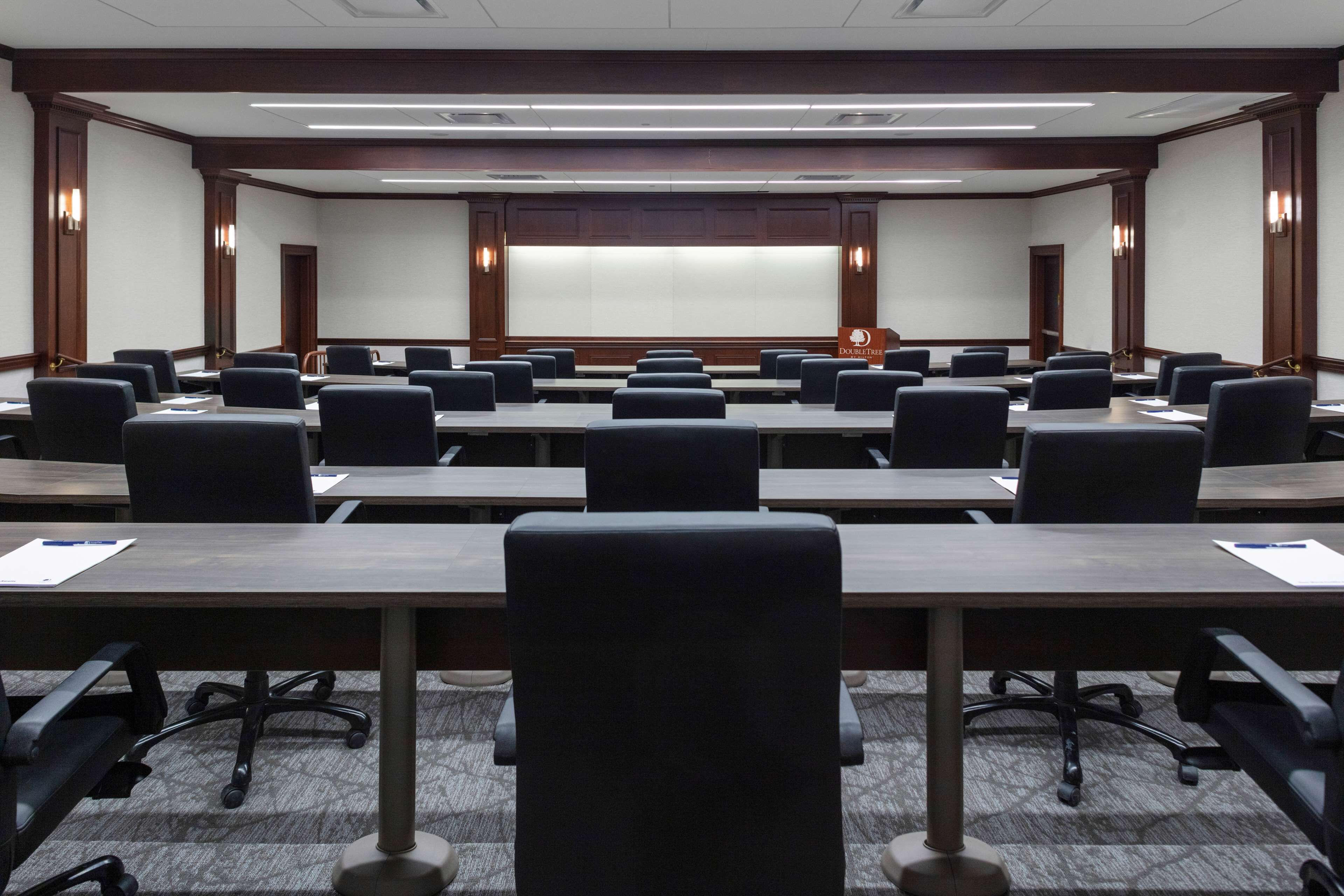 A conference room with multiple tables and chairs, a large screen at the front, and wooden paneling on the walls.