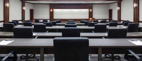 A conference room with multiple tables and chairs, a large screen at the front, and wooden paneling on the walls.