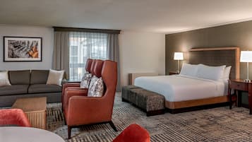 A hotel room with a sofa, a red armchair, a bed, a nightstand, and a wall-mounted lamp.