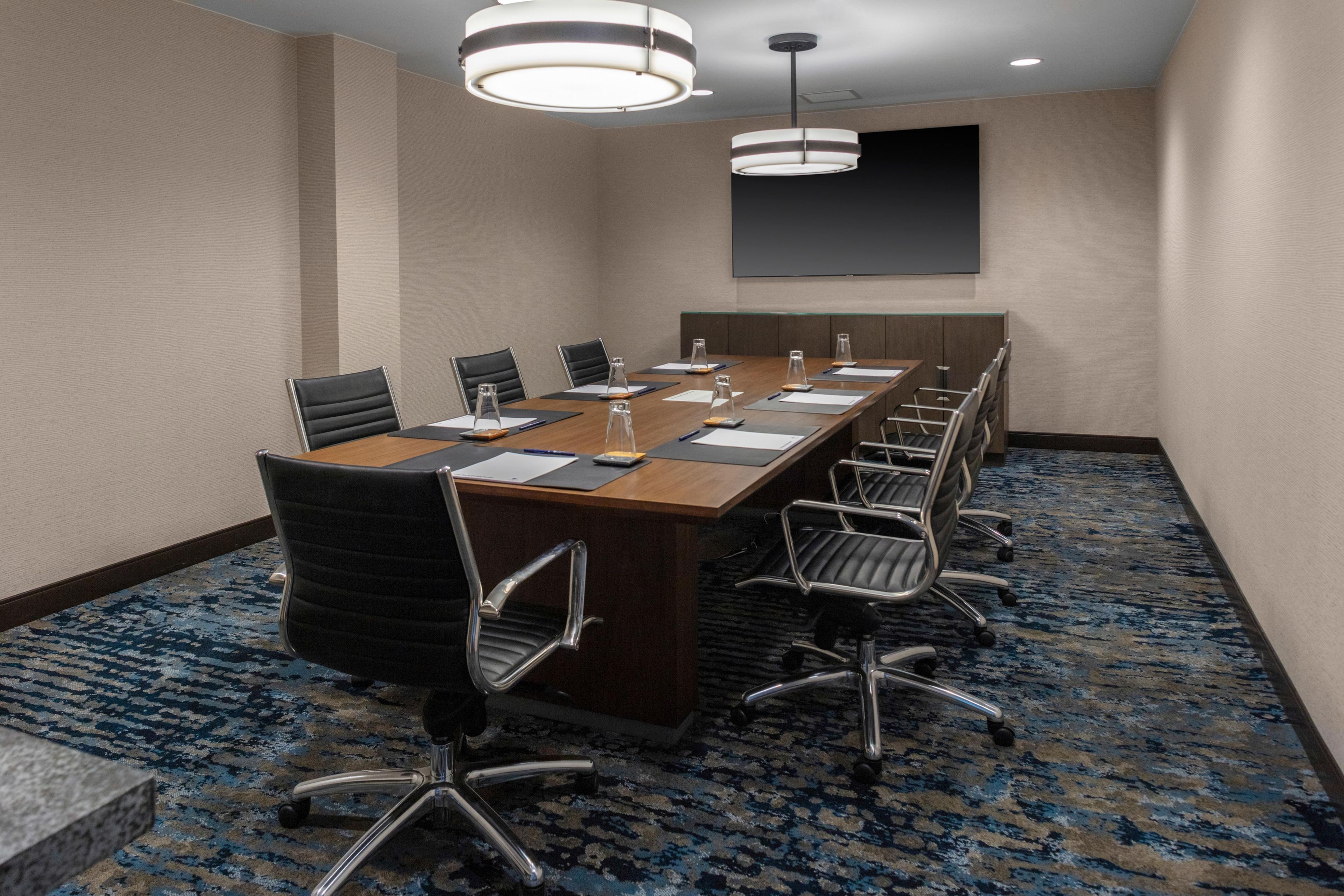 A conference room with a long table, chairs, and a projector screen.