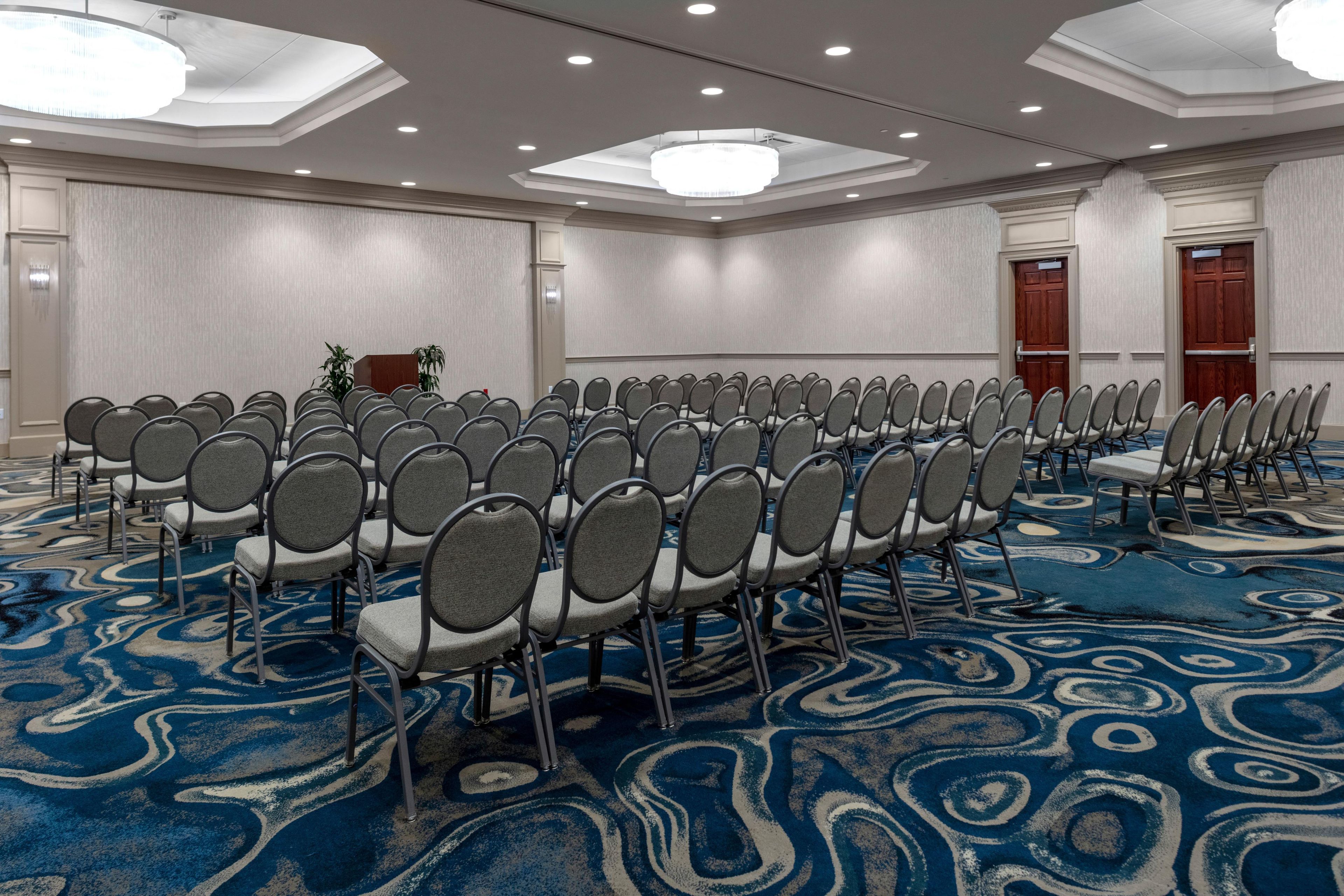 A conference room with rows of chairs, a podium, and a carpeted floor.