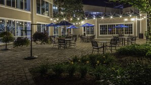 Un espace extérieur aménagé en terrasse, avec des tables et des chaises, entouré de plantes et d’arbres.