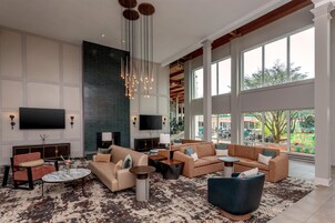 A spacious living area with a large flat-screen TV, multiple seating options, a fireplace, and large windows offering a view of the outdoors.