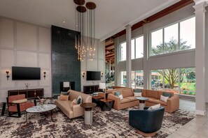 A spacious living area with a large flat-screen TV, multiple seating options, a fireplace, and large windows offering a view of the outdoors. - DoubleTree by Hilton Burlington Vermont (South Burlington)