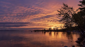A sunset over a calm lake with a rocky shoreline and trees.