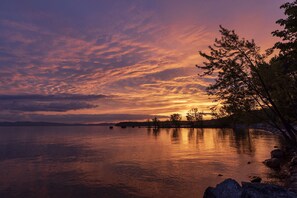 A sunset over a calm lake with a rocky shoreline and trees. - DoubleTree by Hilton Burlington Vermont (South Burlington)