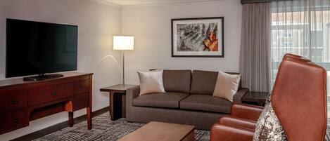 A hotel room with a flat-screen TV, a sofa, a coffee table, and a lamp.