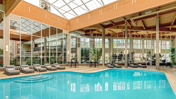 Une grande piscine intérieure dotée de chaises longues et de tables, entourée de grandes fenêtres et de poutres en bois.