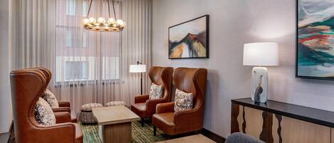 Habitación de hotel con zona de estar, una mesa, una lámpara y obras de arte en las paredes.