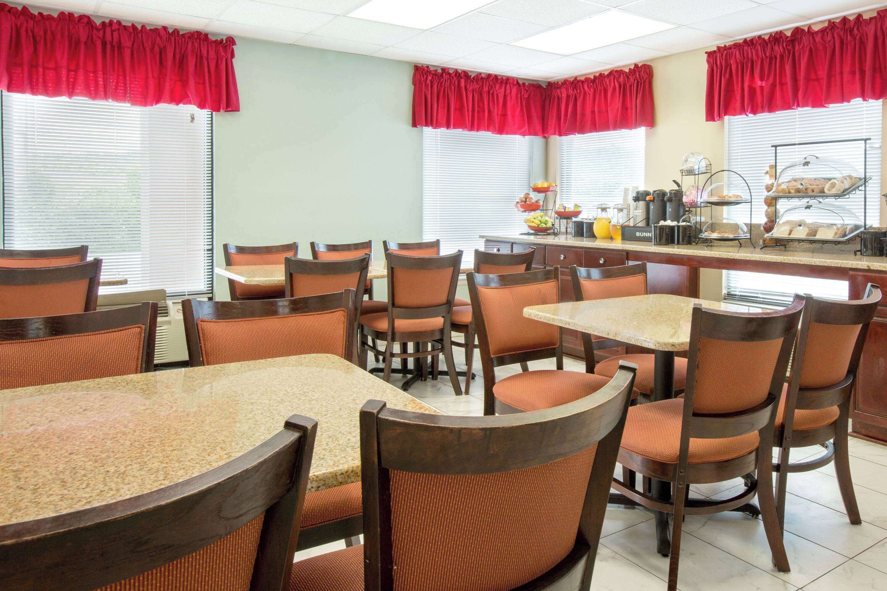 A dining area with multiple tables and chairs, a buffet counter with food and beverages, and red curtains on the windows.
