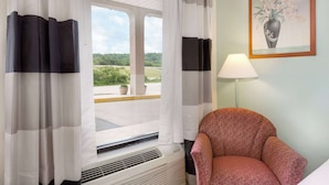 Una habitación con ventana, una silla, una lámpara y un cuadro en la pared.