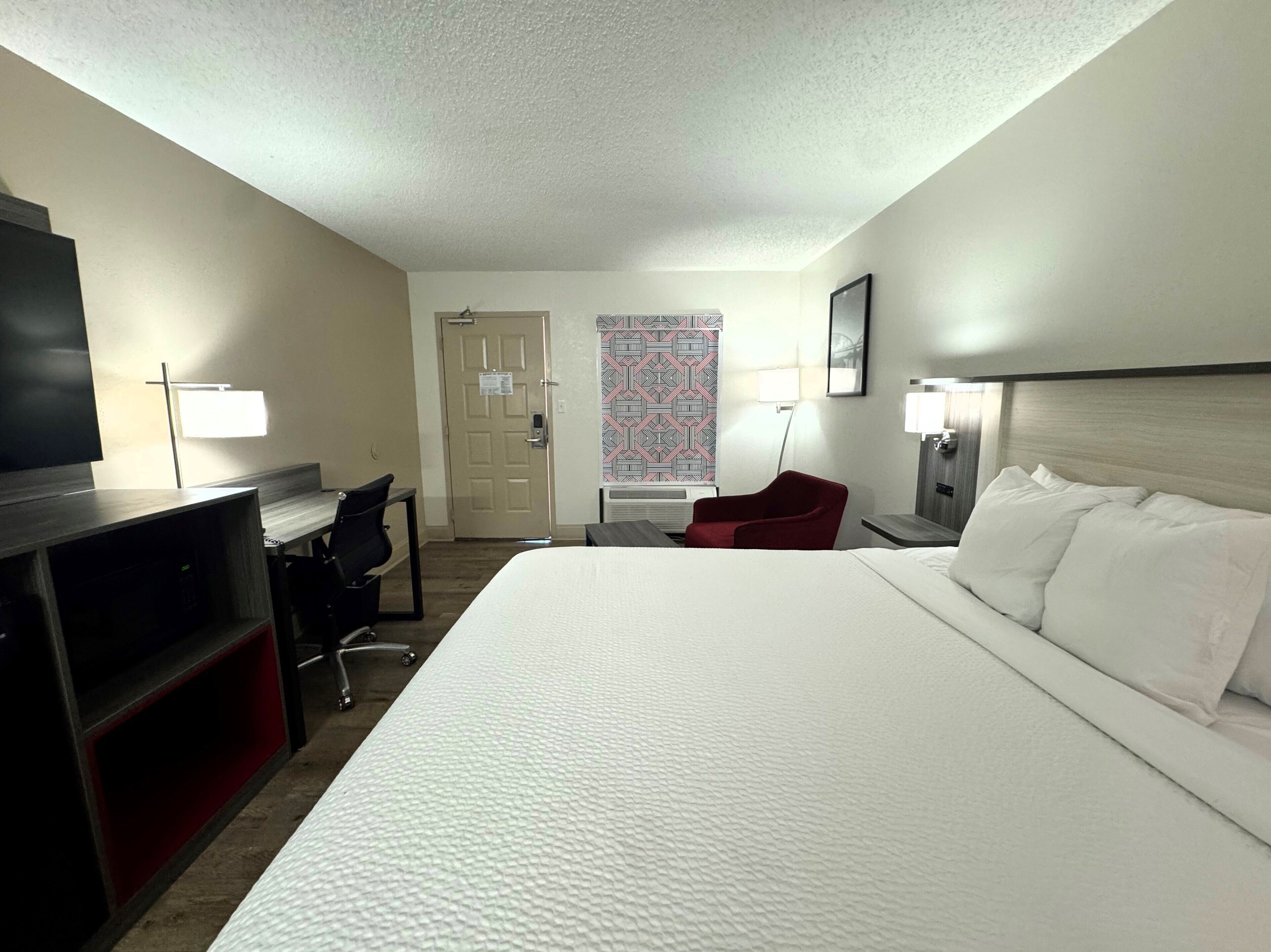 A hotel room with a large bed, a desk with a chair, a TV, and a door.