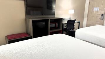 Une chambre d’hôtel avec deux lits, un téléviseur à écran plat fixé au mur, un bureau avec un ordinateur, un four à micro-ondes et une chaise.