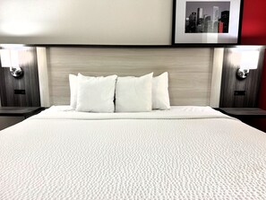 A hotel room with a large bed, two bedside tables, a headboard, and a framed picture on the wall. - Ramada by Wyndham Pelham (Pelham)