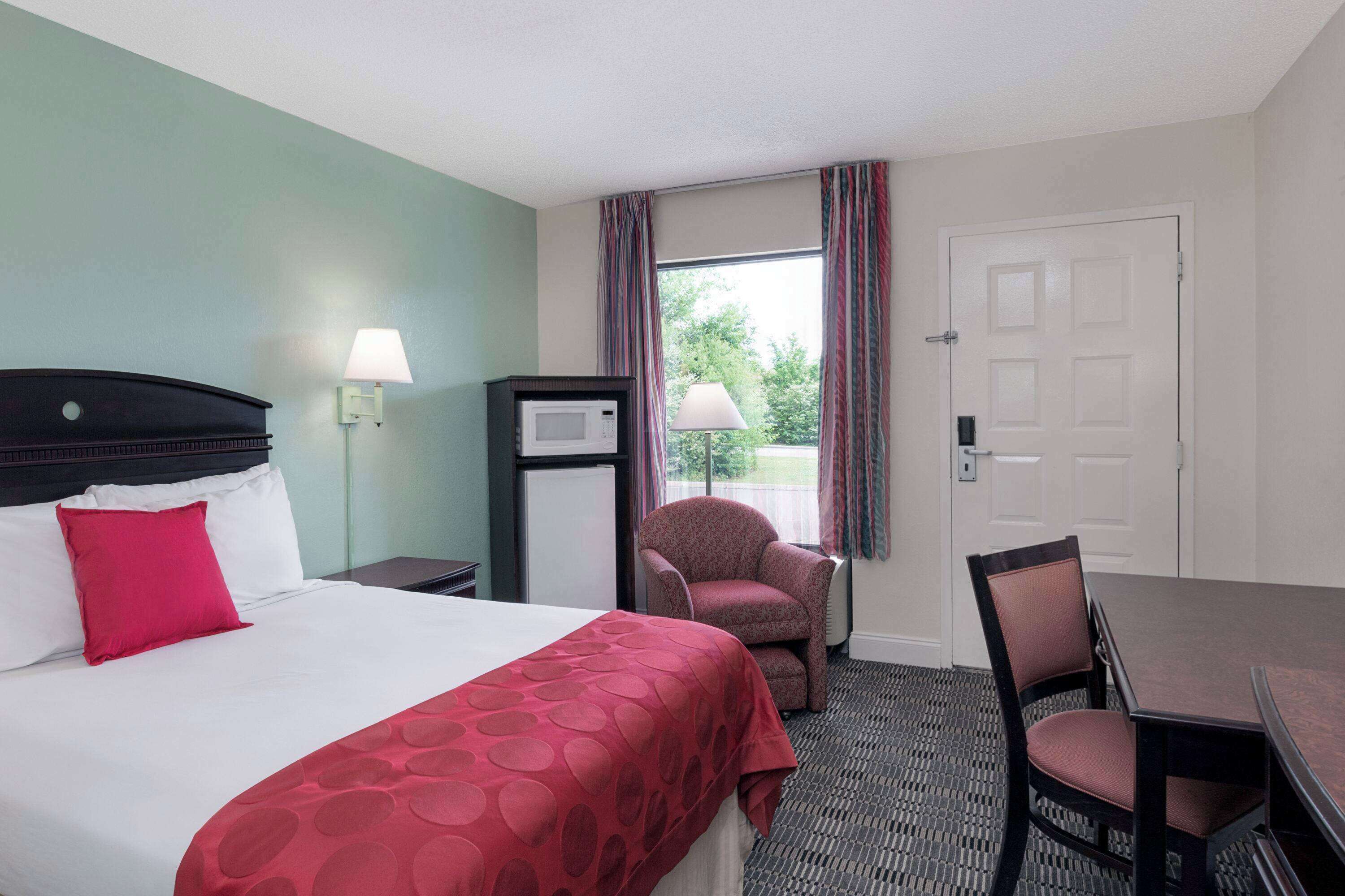 Ein Hotelzimmer mit Bett, Schreibtisch, Stuhl, Lampe, Mikrowelle und Blick ins Freie.