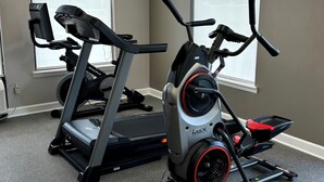 Dos bicicletas estáticas en una habitación con ventana y un reloj de pared.