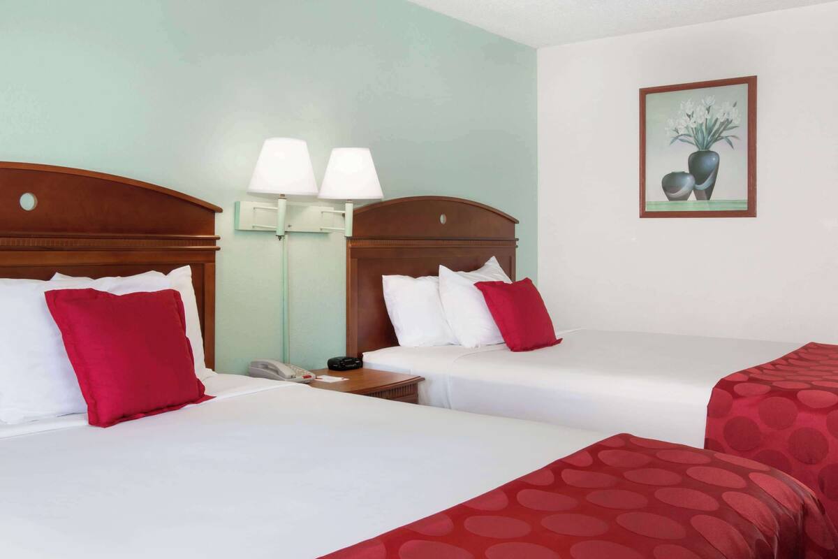 A hotel room with two beds, each with white and red bedding, a nightstand with a lamp, and a painting on the wall.