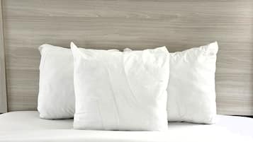 A bed with white bedding and pillows against a wooden headboard.