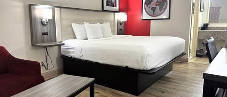 A hotel room with a bed, a desk, a chair, and a red accent wall.