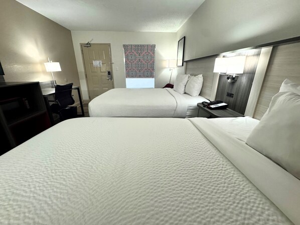 A hotel room with two beds, a desk, a chair, and a door.