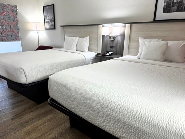 A hotel room with two beds, a bedside table with a lamp, a phone, and a framed picture on the wall.