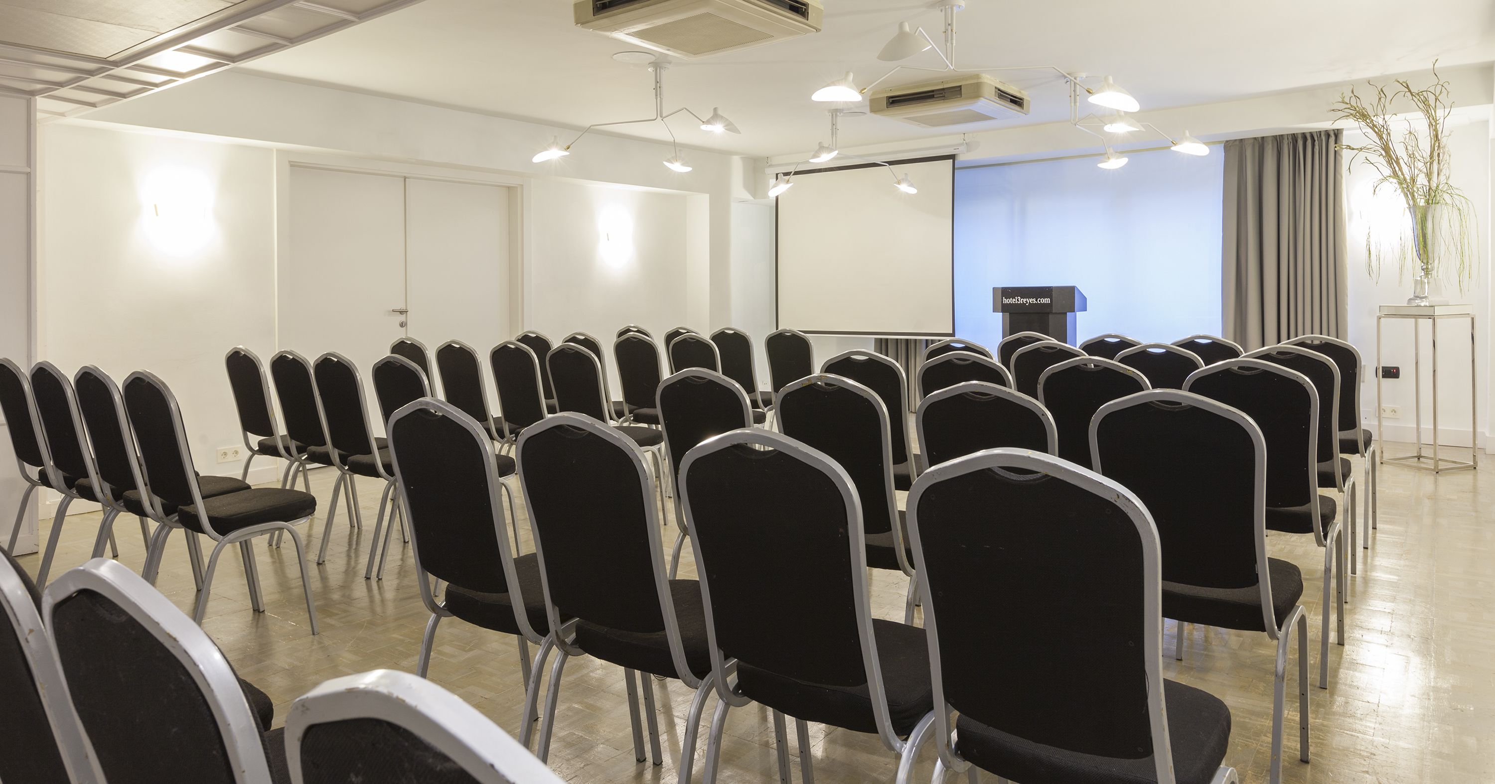 Un salón de conferencias con filas de sillas negras, un atril y una pantalla grande.
