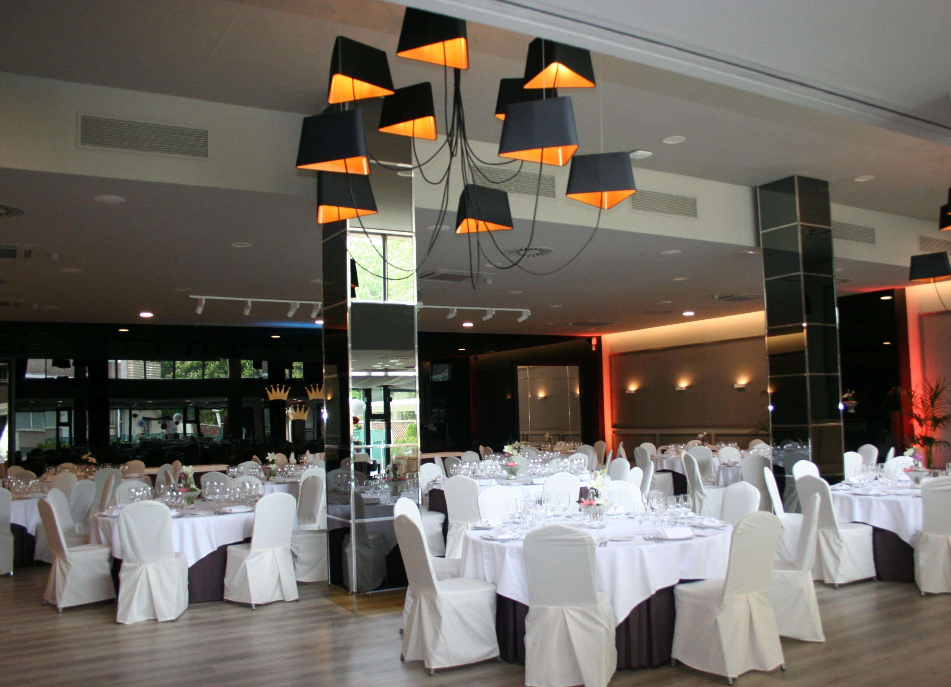 A banquet hall with round tables set for a formal event, featuring white tablecloths and chairs, and modern pendant lighting.