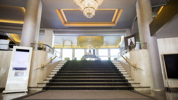 A grand staircase with a chandelier, leading to a lobby area with a large window and a signboard. - Hotel Tres Reyes Pamplona (Pamplona)