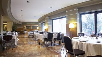 Un amplio comedor con varias mesas y sillas, un letrero de restaurante al fondo y grandes ventanales que dejan entrar luz natural.