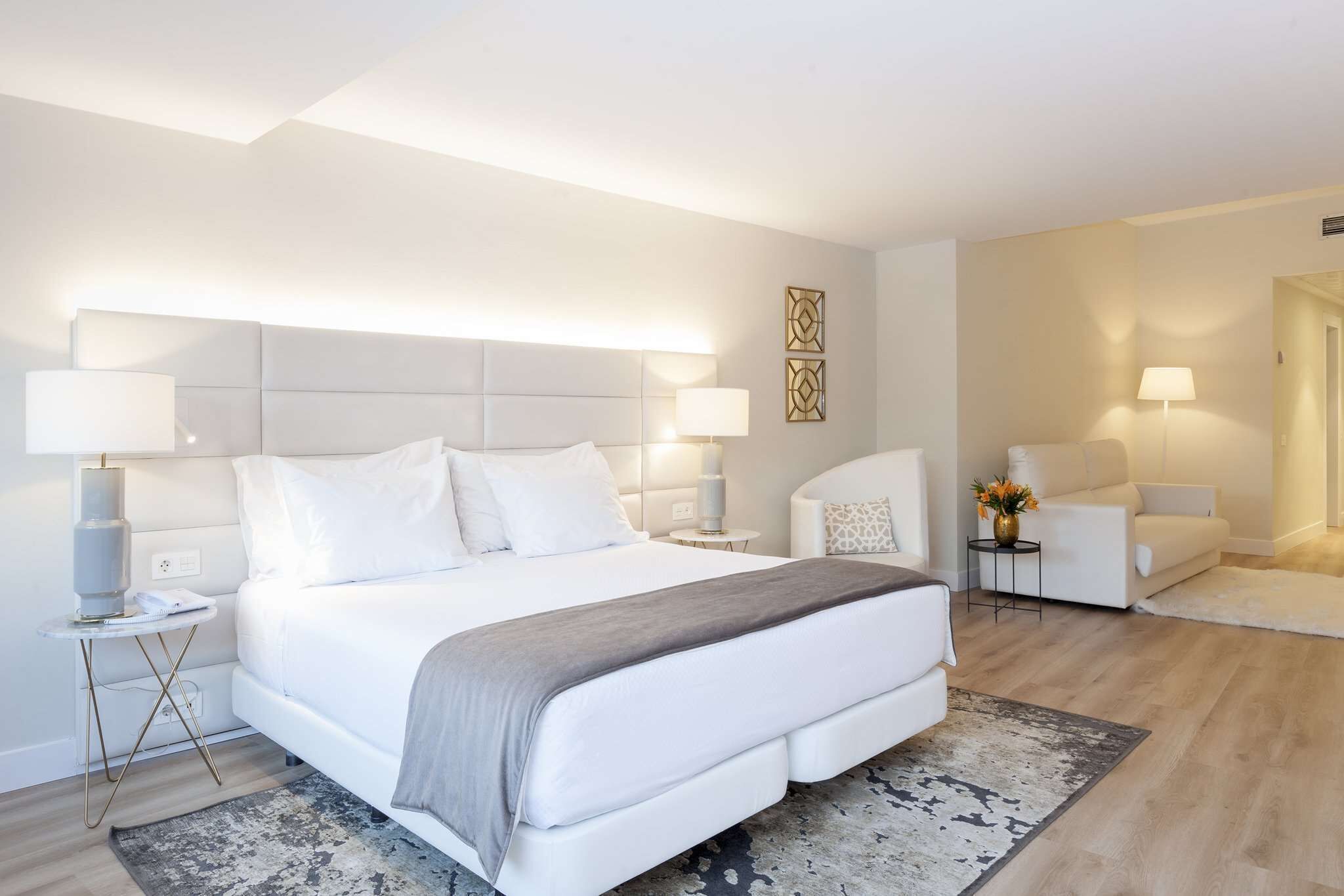 Una habitación de hotel moderna con una cama grande, mesitas de noche, un espacio para sentarse y un adorno de pared.