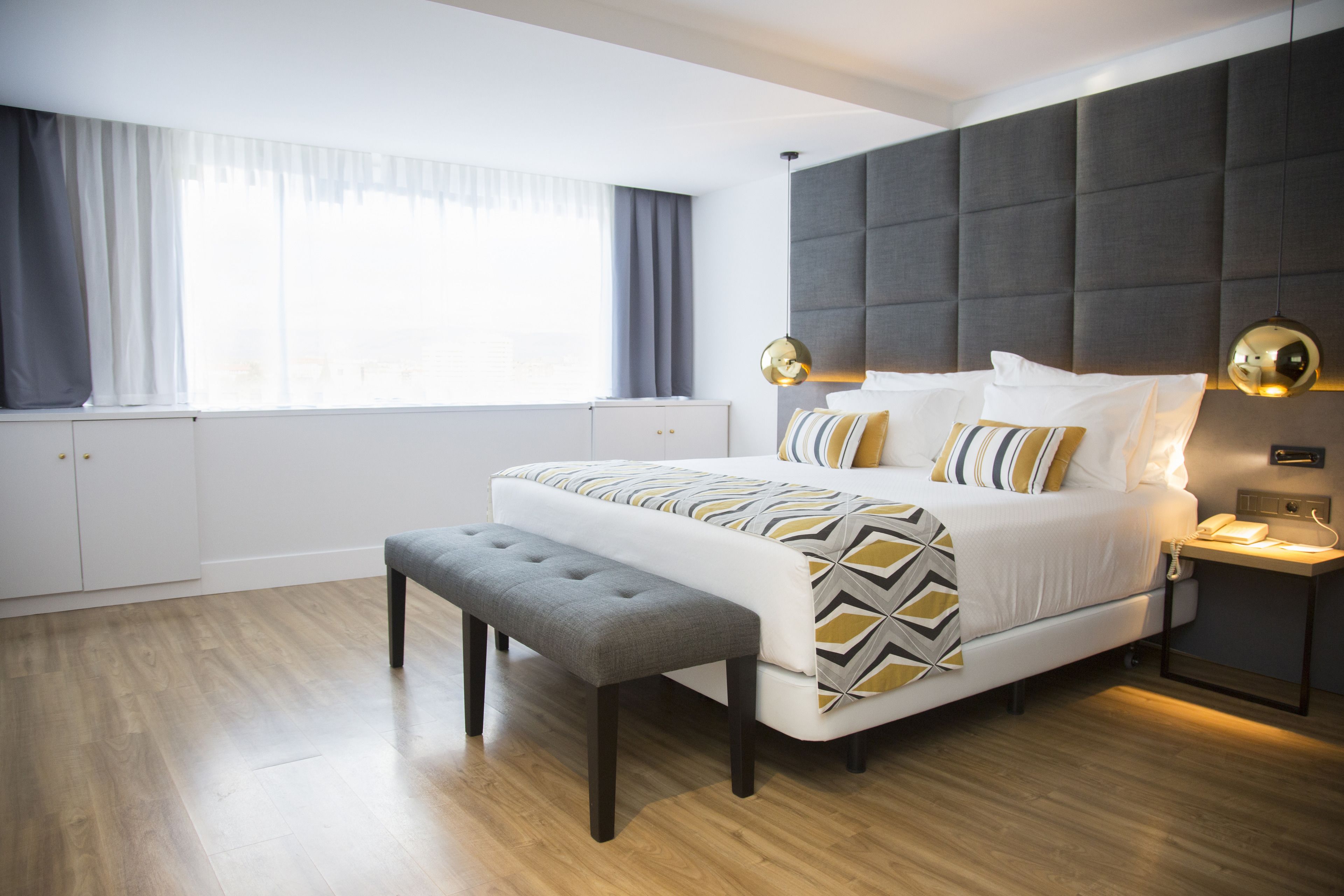 A modern bedroom with a large bed, a bench, a bedside table with a lamp, and a wardrobe.