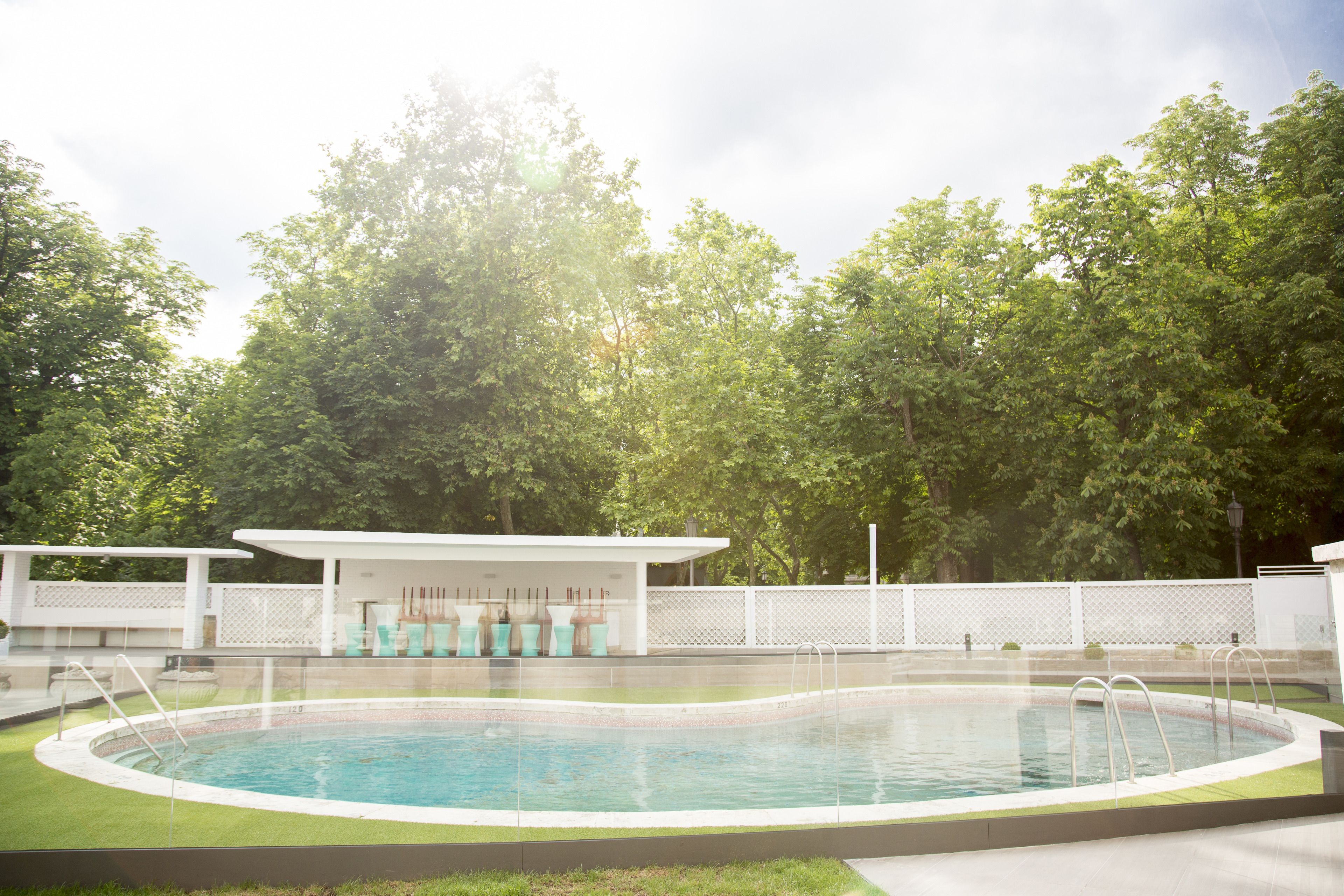 A swimming pool with a covered seating area and a white fence.