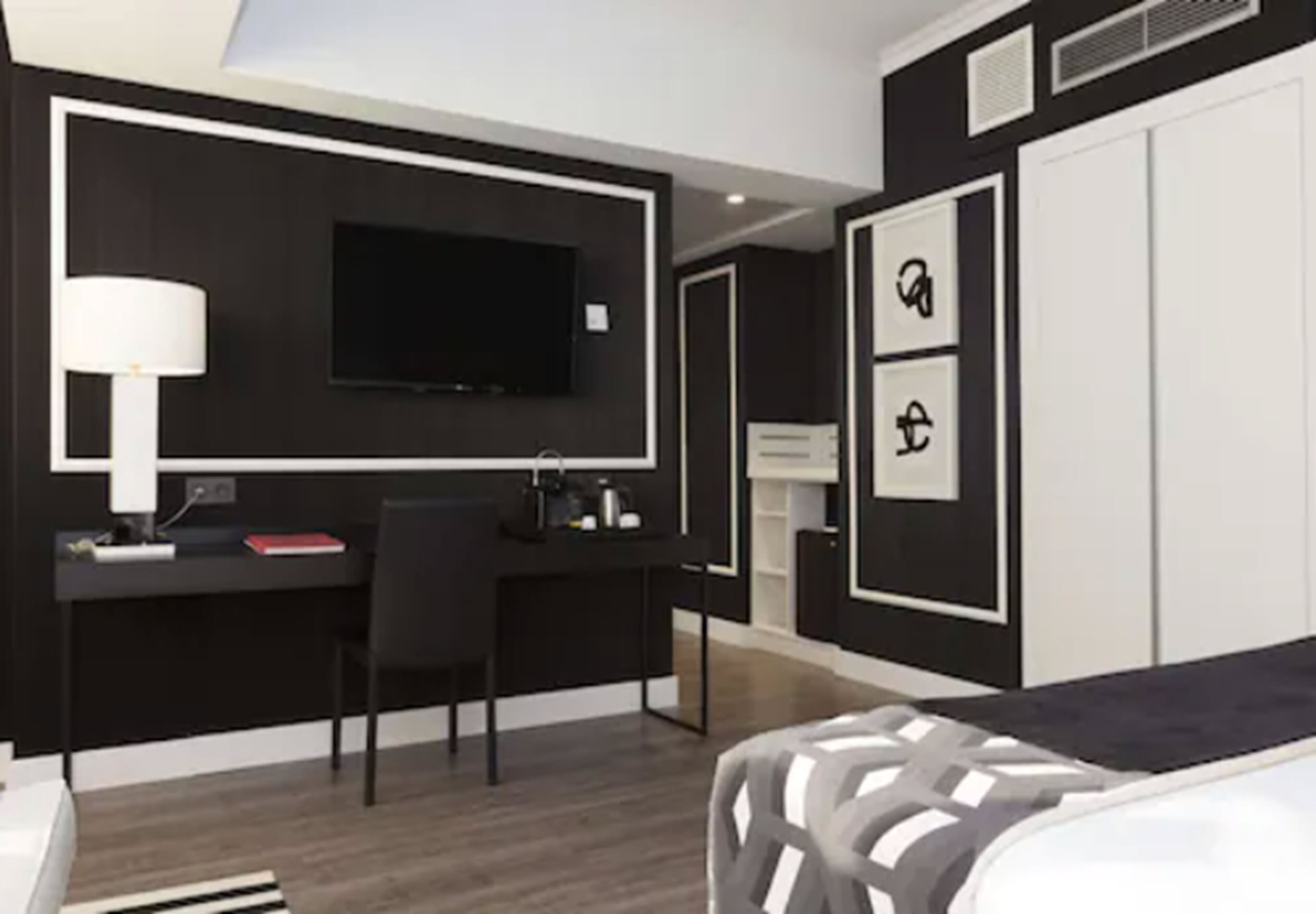 Une chambre d’hôtel moderne aux couleurs noir et blanc, dotée d’un téléviseur à écran plat, d’un bureau avec une chaise et d’un lit avec une tête de lit à motifs.