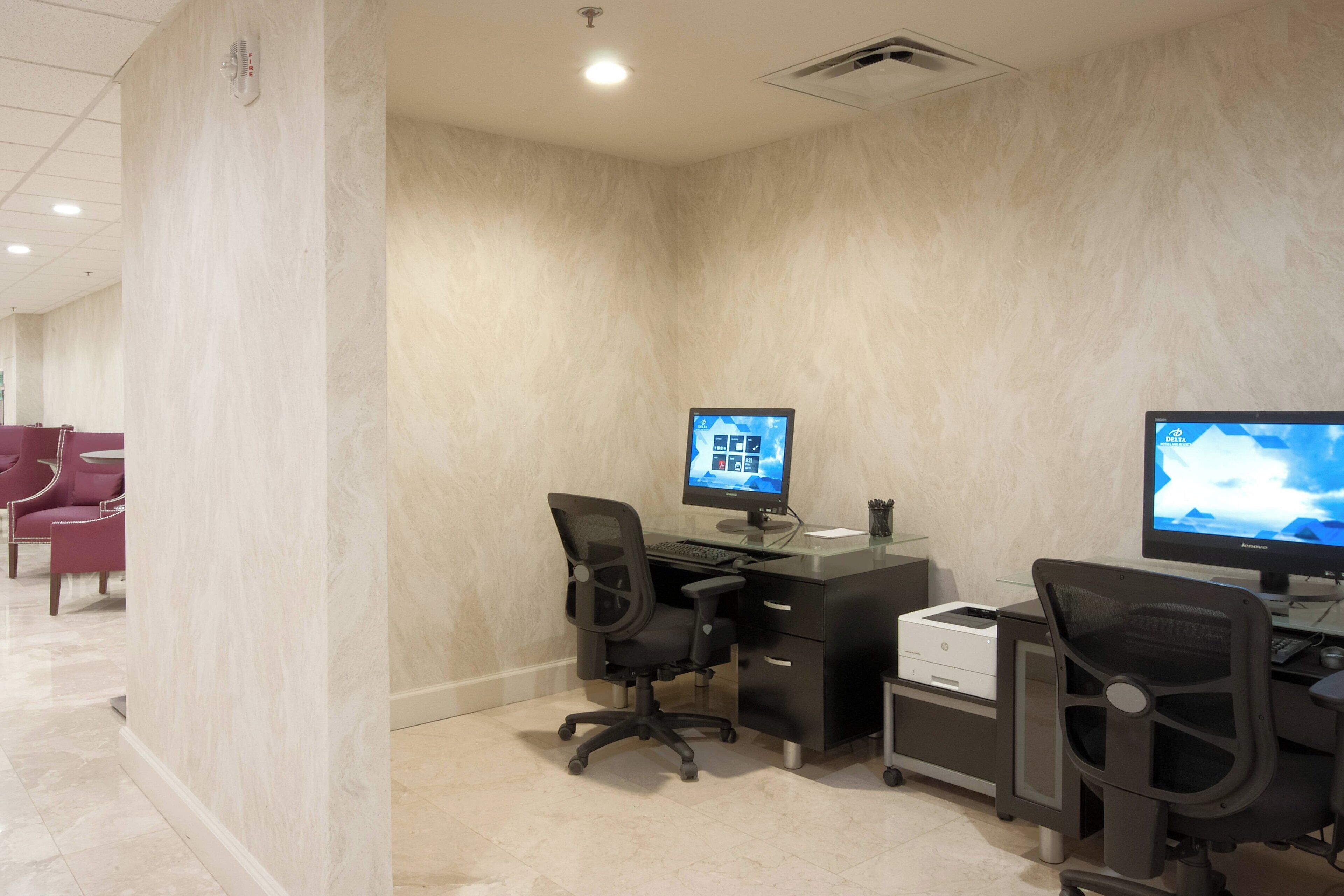 A modern office space with two desks, each with a computer monitor, black office chairs, and a printer.