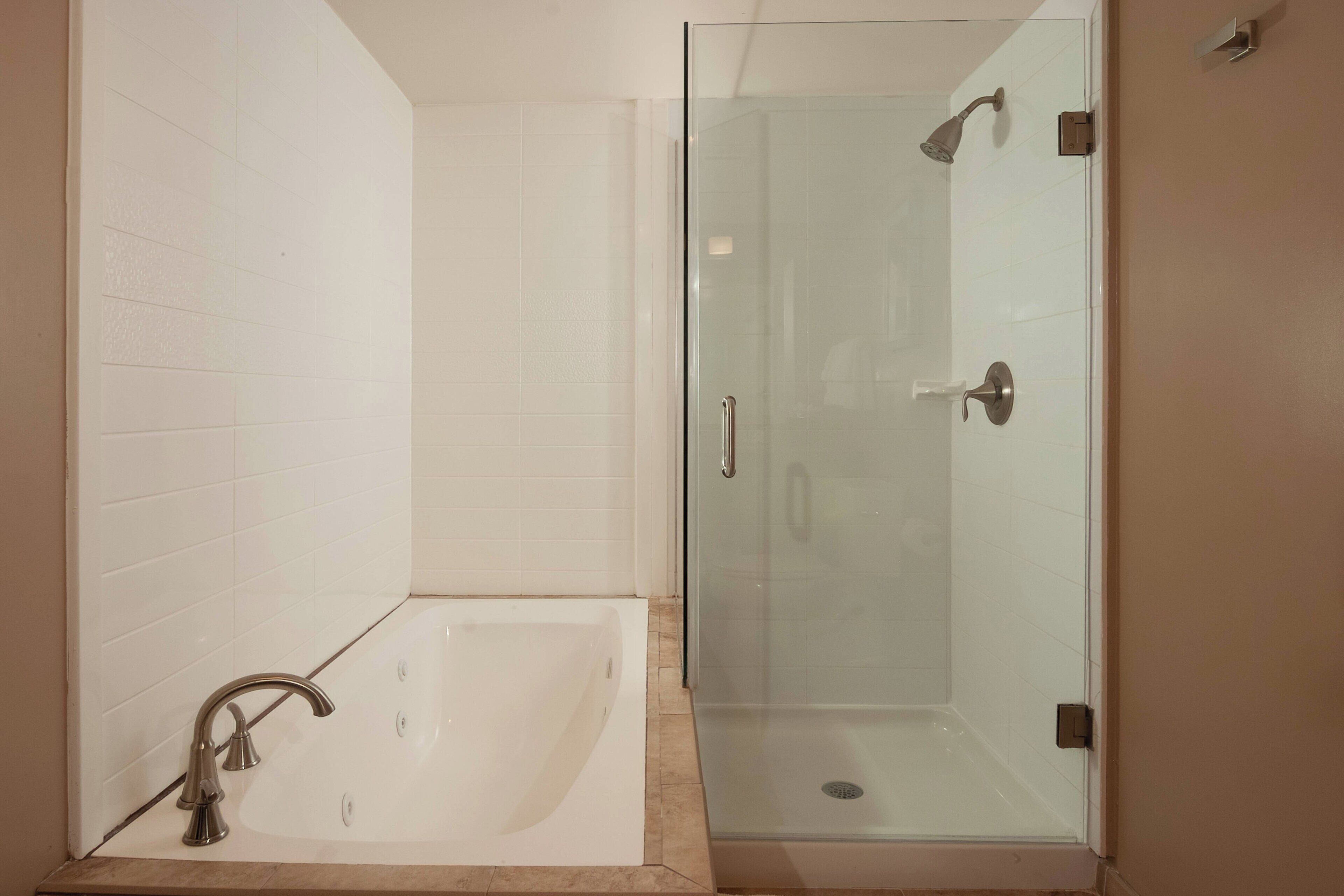 Une salle de bain avec une douche à parois de verre, une baignoire et des murs recouverts de carreaux blancs.