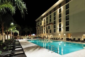 Una piscina con sillas de descanso y un edificio de varios pisos con balcones.