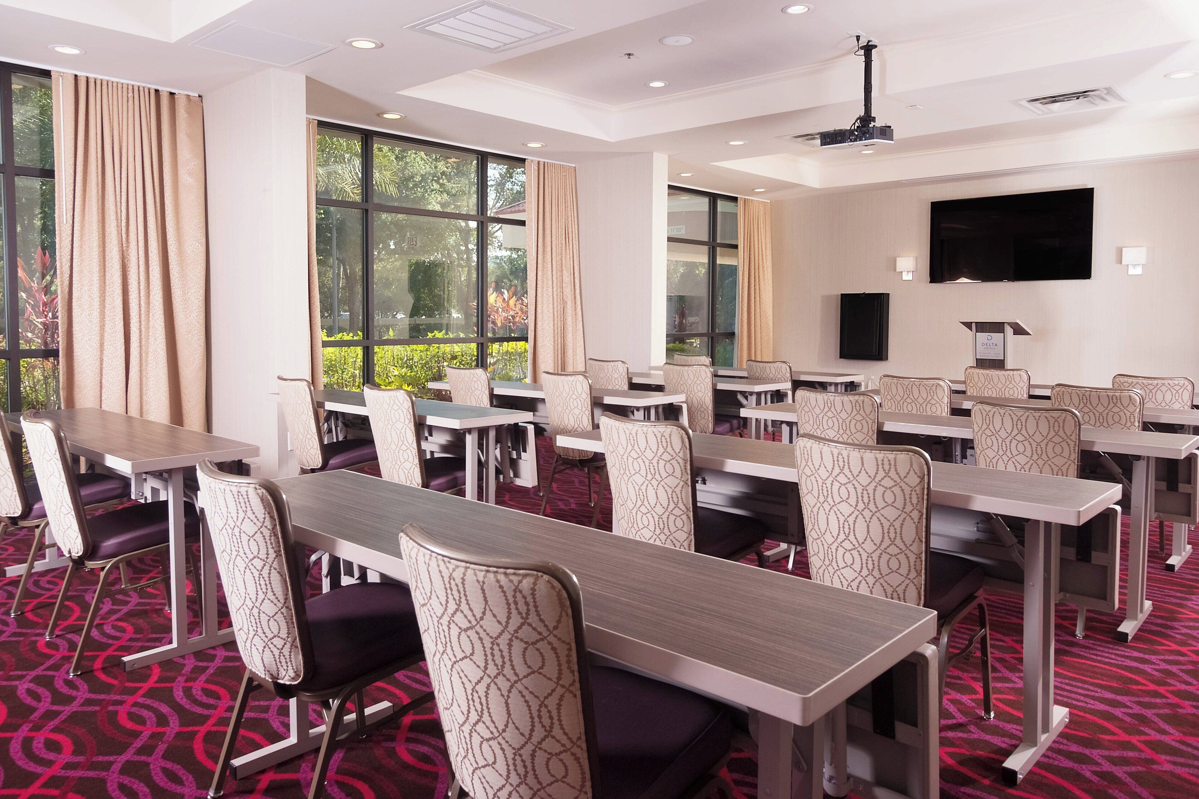 A conference room with multiple tables and chairs, large windows with curtains, a flat-screen TV, and a projector.