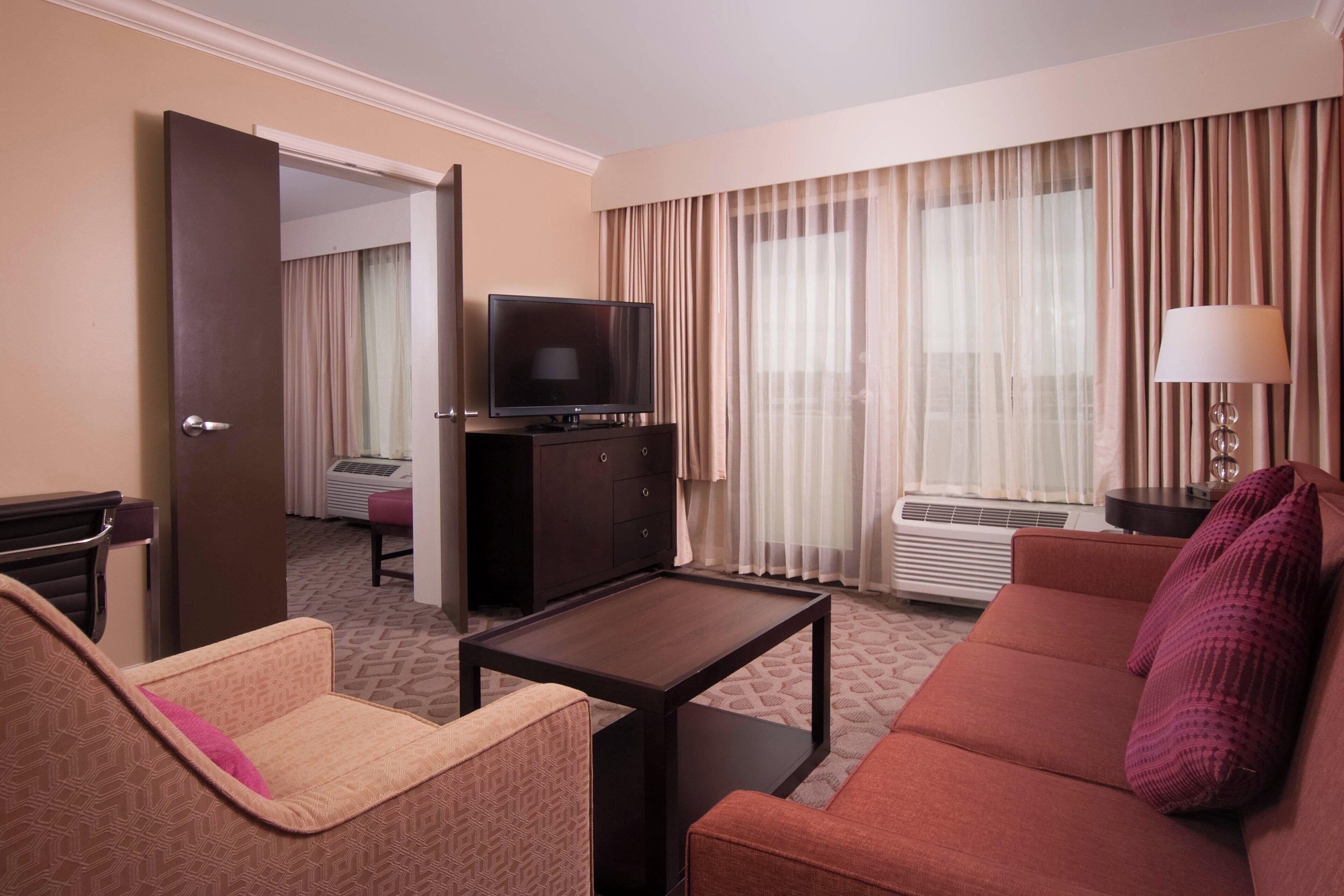 Habitación de hotel con sofá, una mesita, televisor, lámpara y ventana con cortinas.
