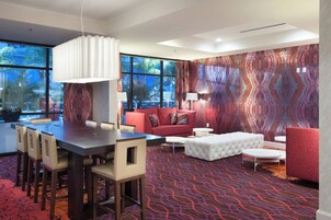 Una camera d'albergo moderna con angolo ristoro, un divano rosso, un poggiapiedi bianco e una moquette fantasia.