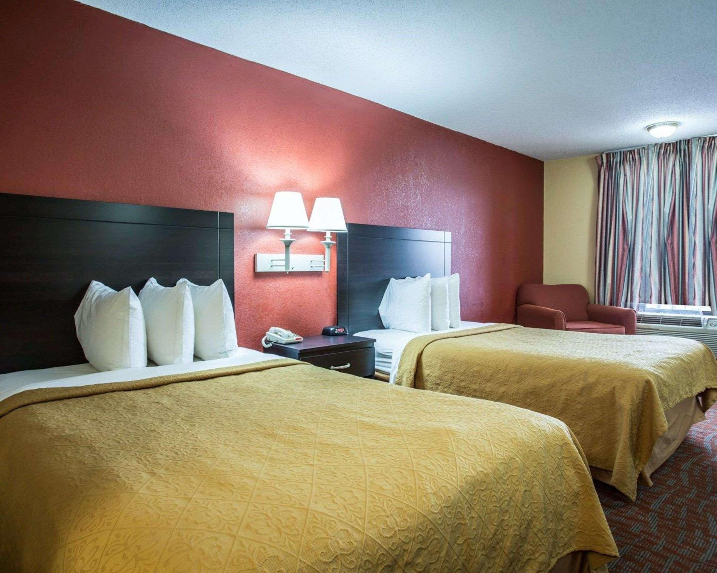 Ein Hotelzimmer mit zwei Betten, einem Nachttisch, einem Sessel und einem Fenster mit Vorhängen.