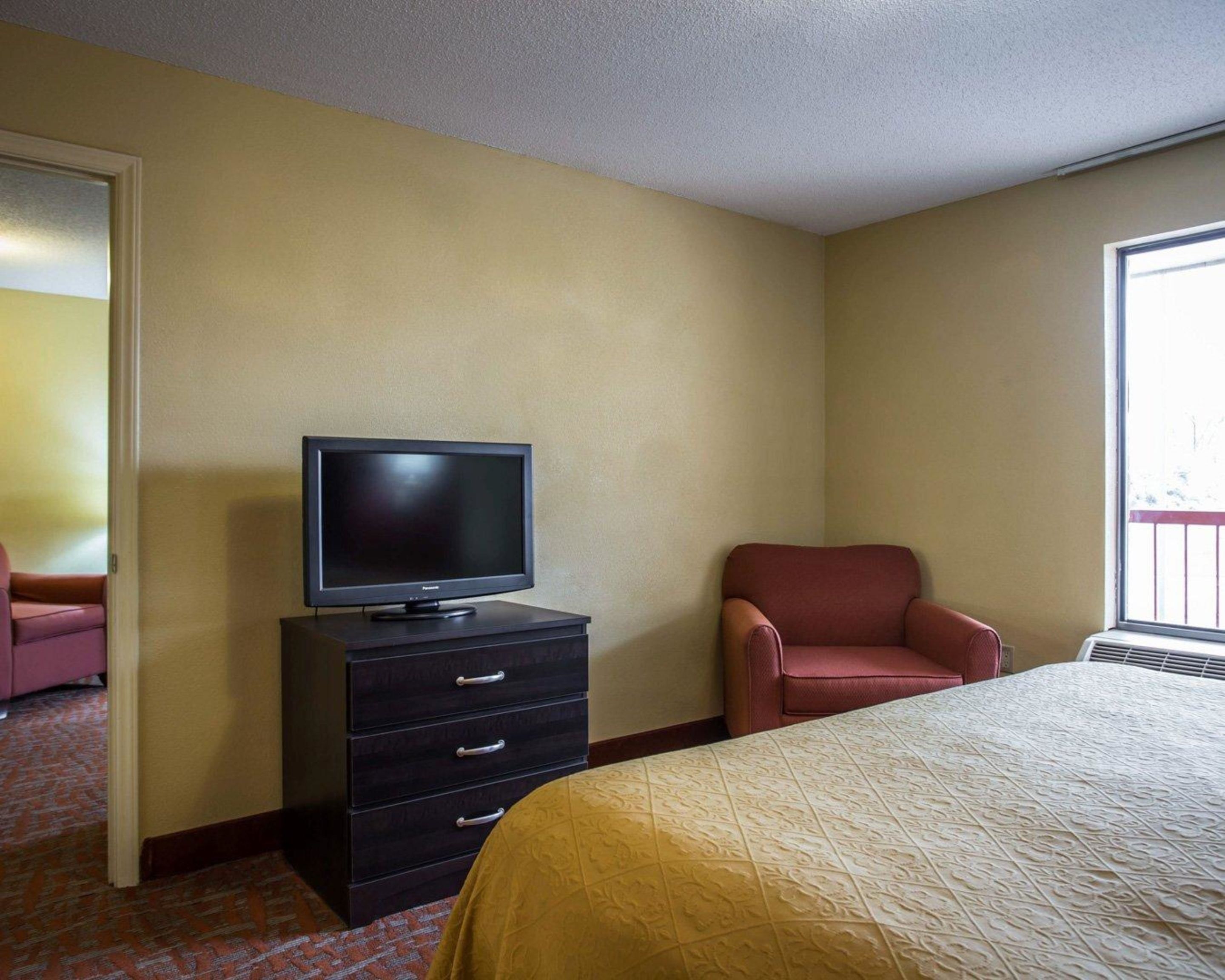 A hotel room with a bed, a television on a dresser, a chair, and a window.