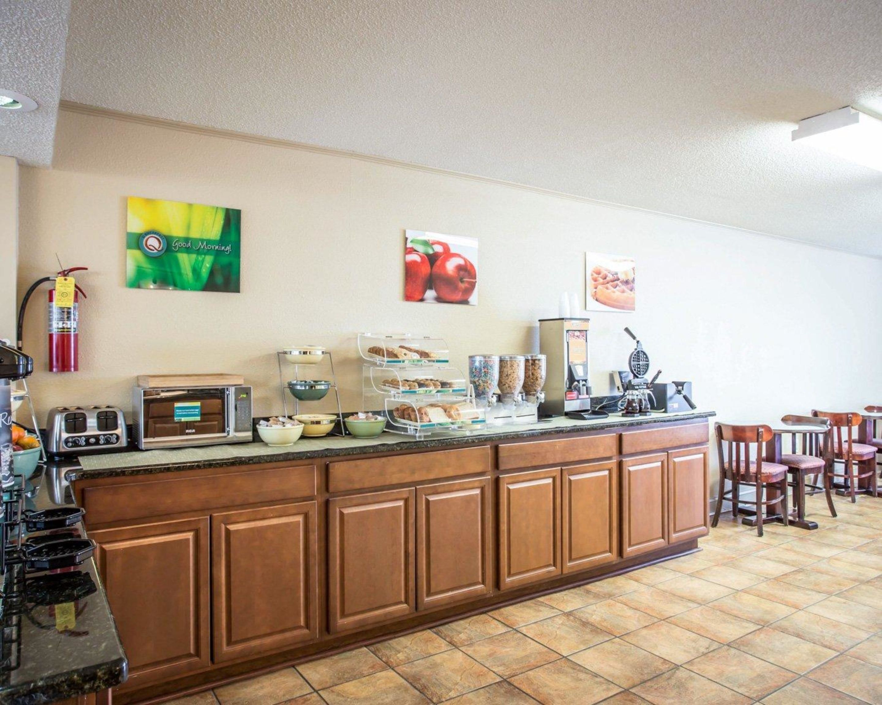 A breakfast bar with various food items and a coffee machine. There are chairs and a fire extinguisher on the wall.